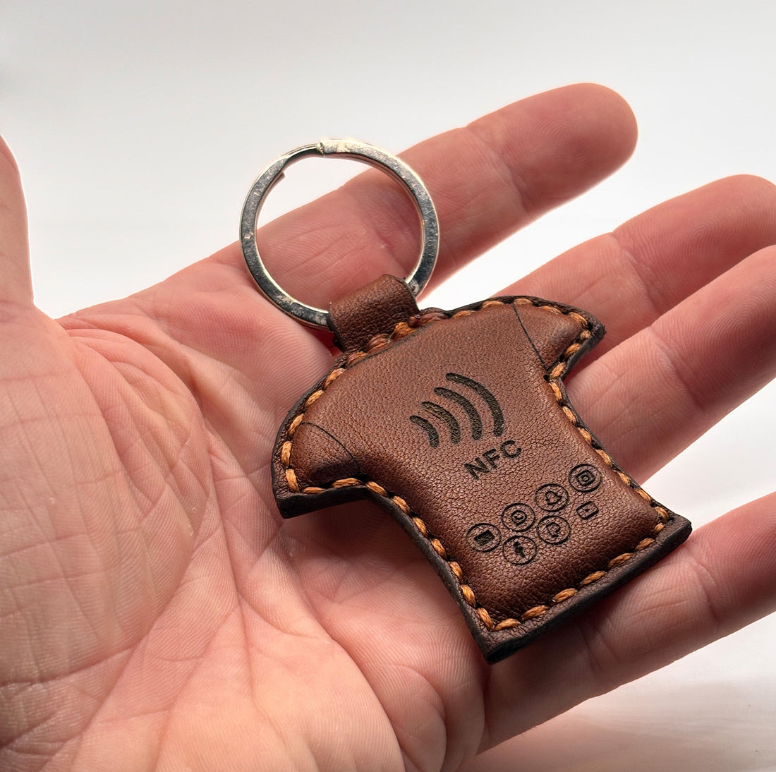 Hand hält braunen NFC-Schlüsselanhänger aus Leder mit eingraviertem NFC-Symbol – moderne digitale Visitenkarte von EngelzKind.